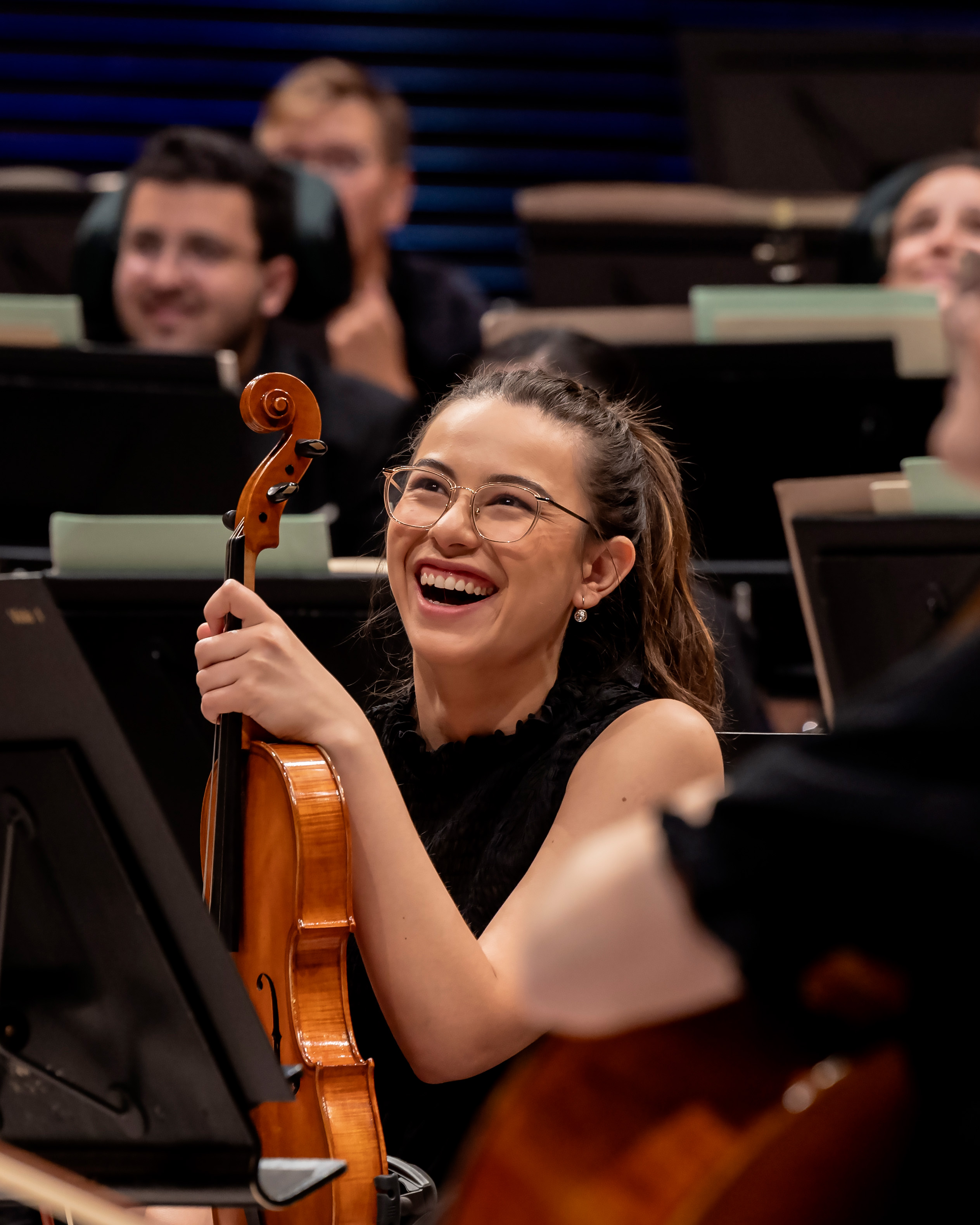 A female student wearing a red dress, playing the violin in a crowd.